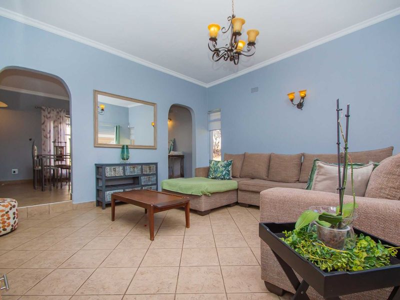 A comfortable living room featuring tiled flooring, arched architectural transitions to adjacent spaces, and classic wall sconce lighting.