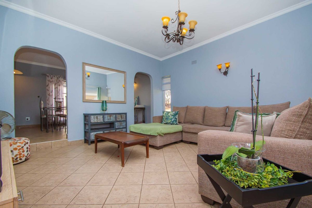 A comfortable living room featuring tiled flooring, arched architectural transitions to adjacent spaces, and classic wall sconce lighting.