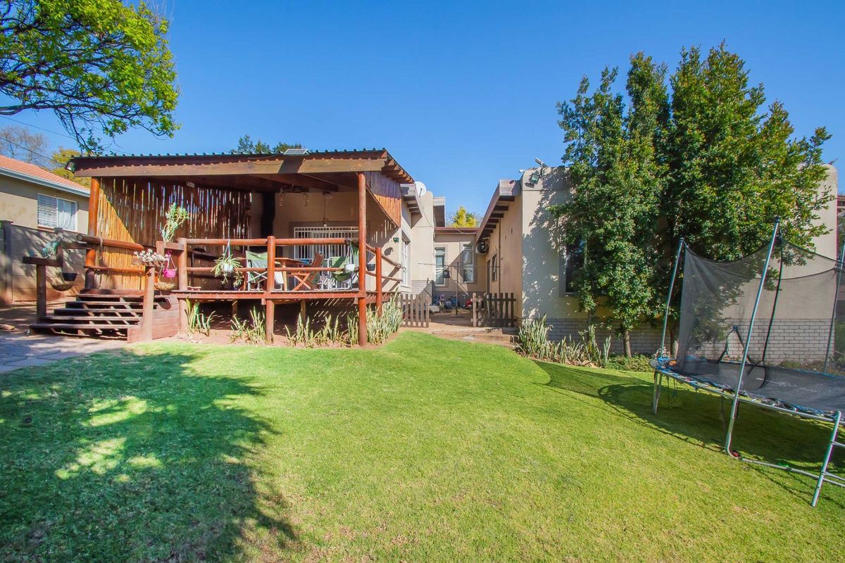 Rear view of the property featuring a raised timber deck with a covered patio area overlooking a well-maintained garden lawn.