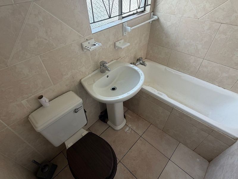 A functional bathroom featuring a pedestal basin, bathtub, and toilet with neutral ceramic tiling throughout.