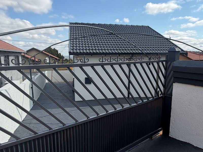 A view of the property entrance featuring a modern metal driveway gate, paved driveway, and a well-maintained tiled roof structure.