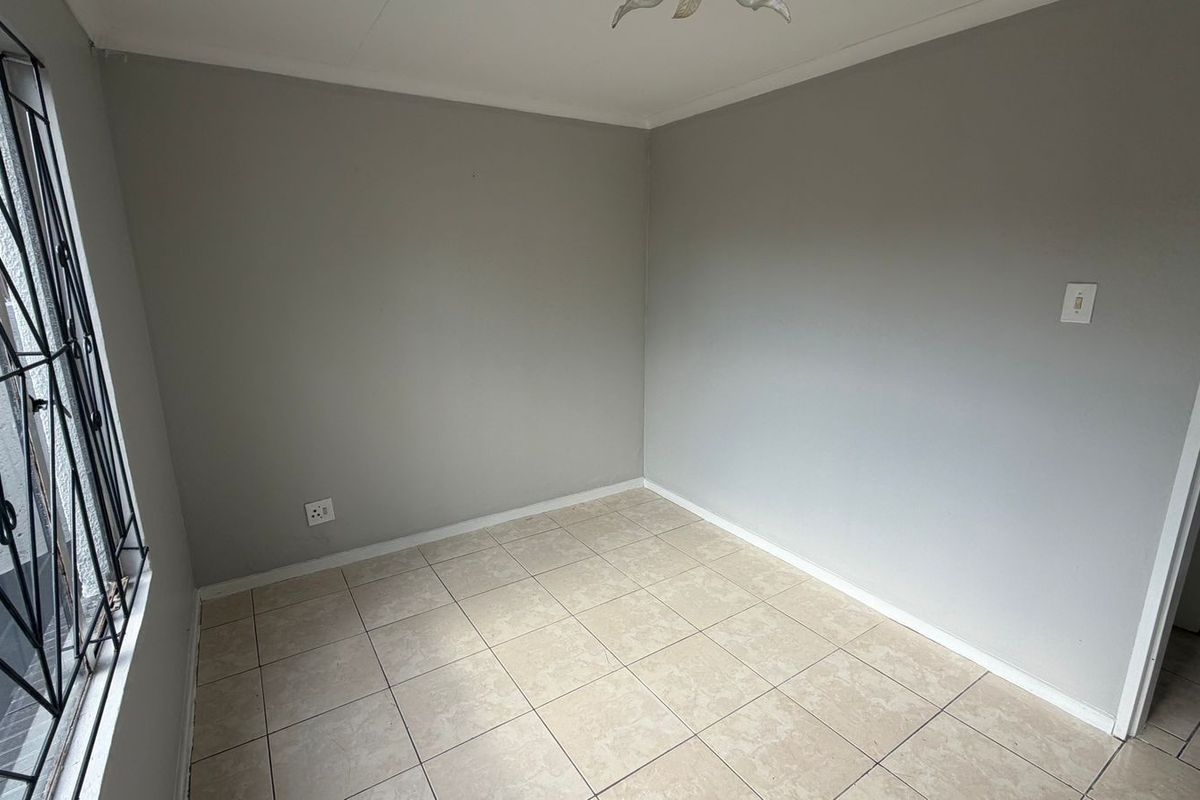 A clean, empty bedroom featuring neutral grey walls, tiled flooring, and a security gate on the window.
