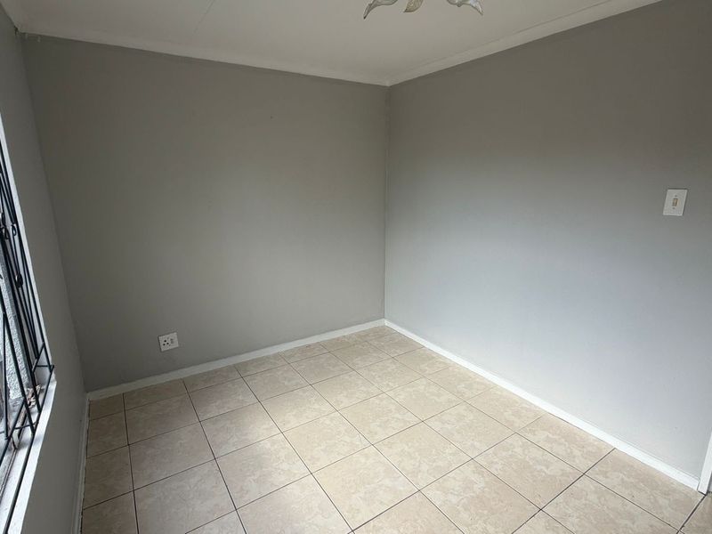 A clean, empty bedroom featuring neutral grey walls, tiled flooring, and a security gate on the window.