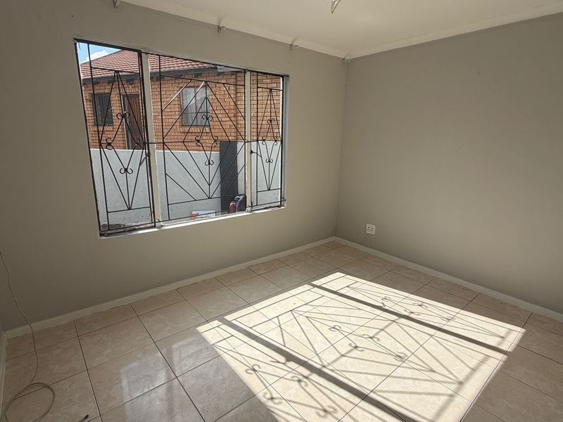 A vacant bedroom featuring neutral wall paint, tiled flooring, and security burglar bars on the window.