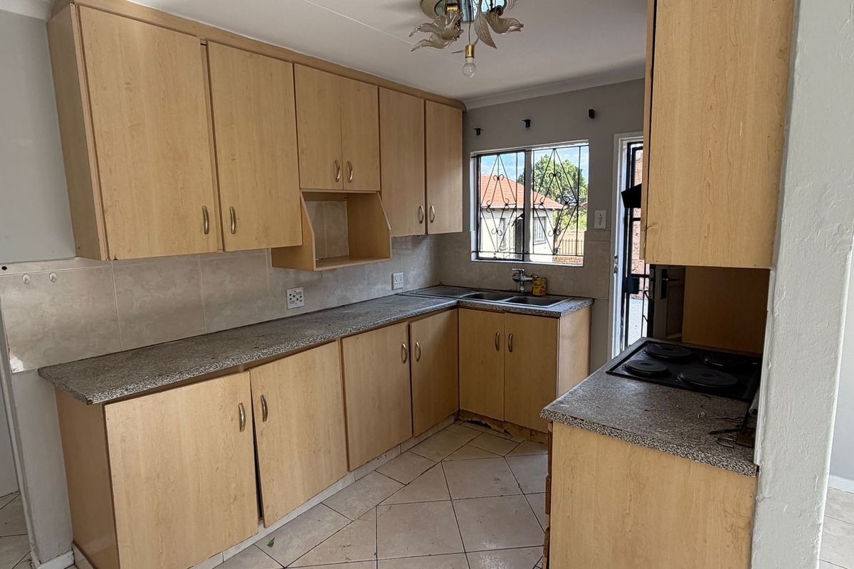 A functional kitchen featuring light wood-finish cabinetry, granite-look laminate countertops, a built-in electric hob, and tiled flooring.