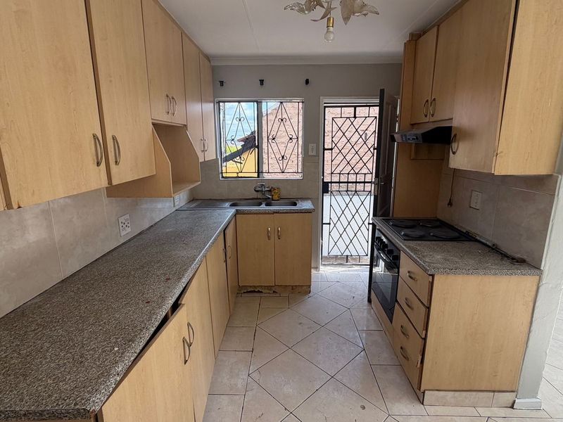 A functional kitchen featuring laminate cabinetry, granite-look countertops, built-in oven and hob, and direct access to the exterior via a security gate.
