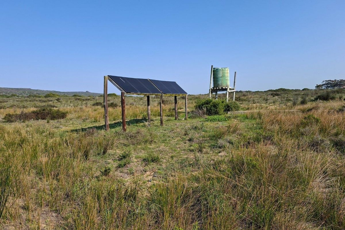 Outdoor utility area featuring a ground-mounted solar panel array and an elevated water storage tank on a timber frame structure.