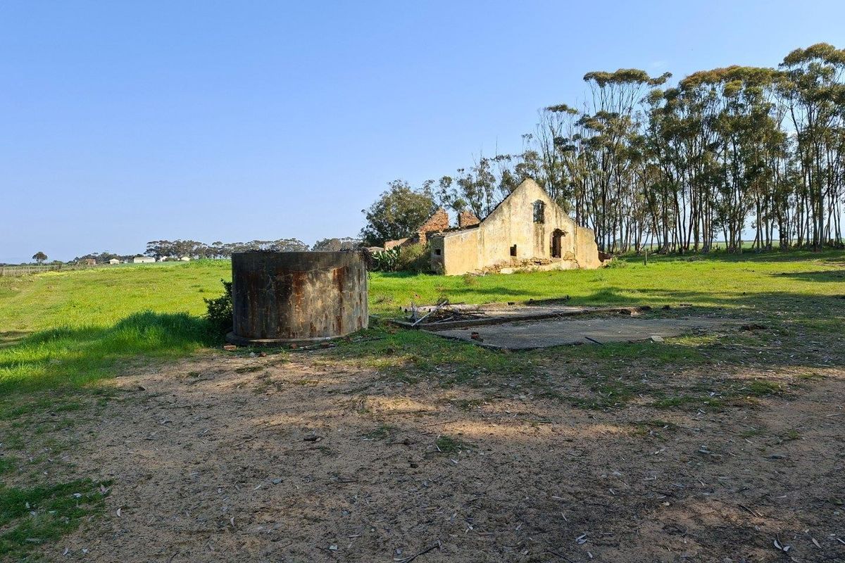A view of a rural farm property featuring a ruined masonry structure, a concrete water reservoir, and an existing concrete slab foundation.