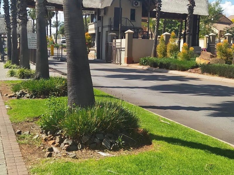 View of the secure estate entrance featuring a thatched gatehouse, paved driveway, and well-maintained landscaped verge.
