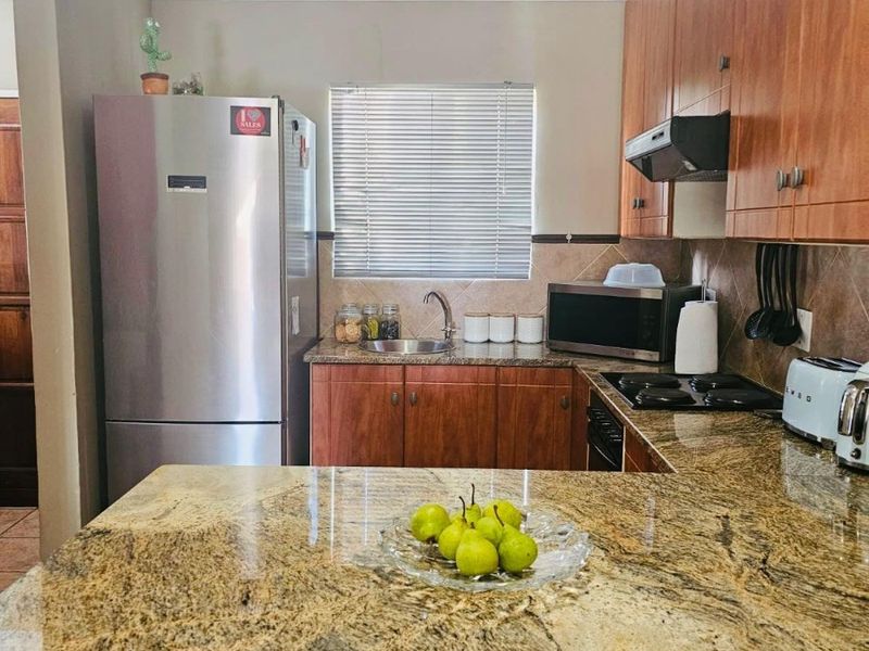A functional kitchen featuring granite countertops, wooden cabinetry, a built-in hob with extractor fan, and a tiled backsplash.