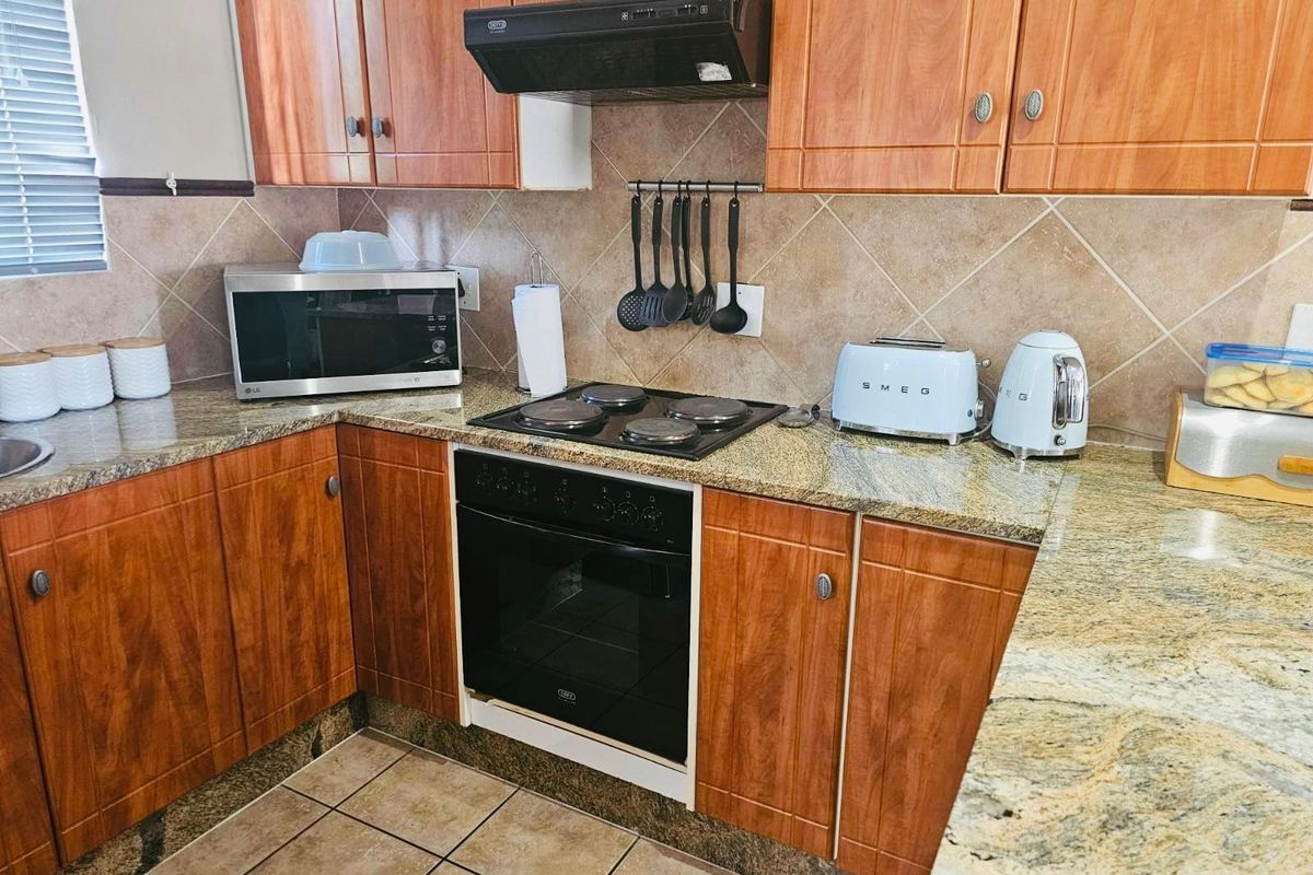 A functional kitchen featuring wooden cabinetry, granite countertops, a built-in oven, electric hob, and a tiled backsplash.