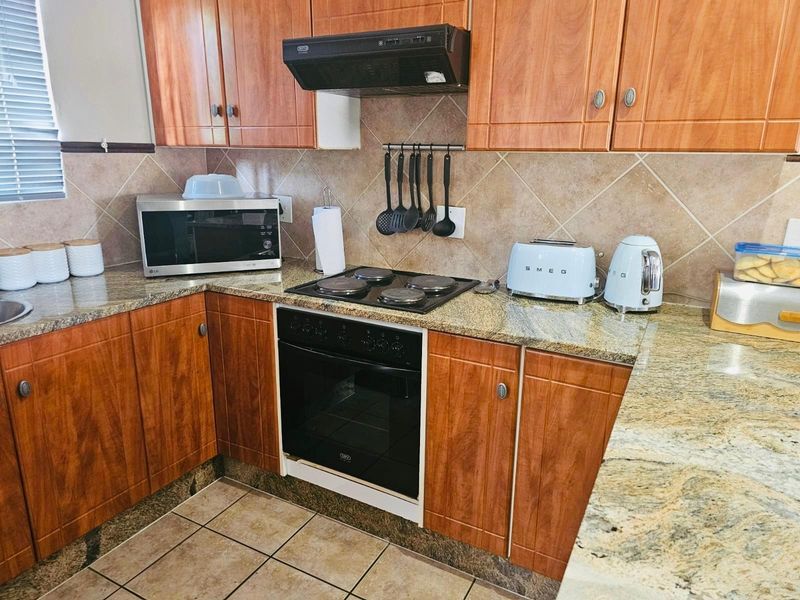 A functional kitchen featuring wooden cabinetry, granite countertops, a built-in oven, electric hob, and a tiled backsplash.