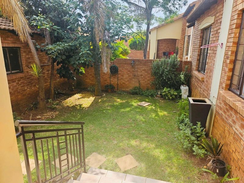 A private rear garden area featuring a lawn, established trees, and brick boundary walls, accessible via a set of tiled steps with metal railings.