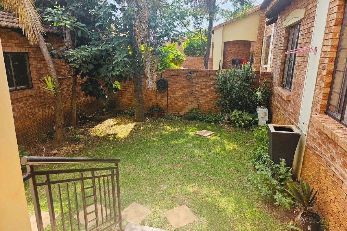 A private rear garden area featuring a lawn, established trees, and brick boundary walls, accessible via a set of tiled steps with metal railings.