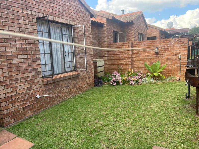 A private rear garden area featuring a well-maintained lawn, face brick exterior walls, and secure window bars.