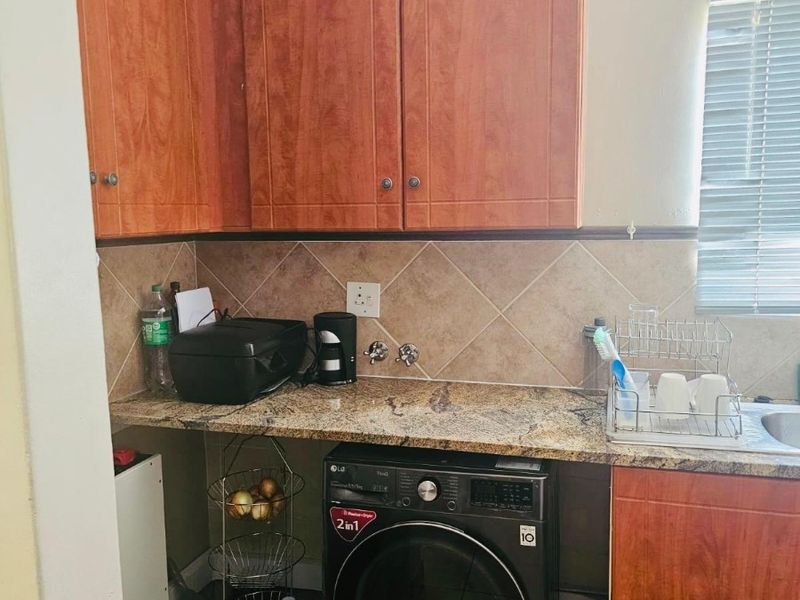 A functional laundry area featuring granite countertops, tiled backsplash, and wood-finish cabinetry with dedicated plumbing for a washing machine.