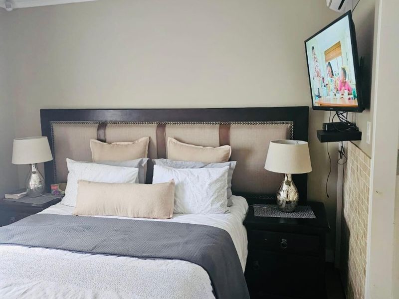 A comfortable bedroom featuring a wall-mounted air conditioning unit and a television mount, with neutral wall tones and tiled accent detailing.