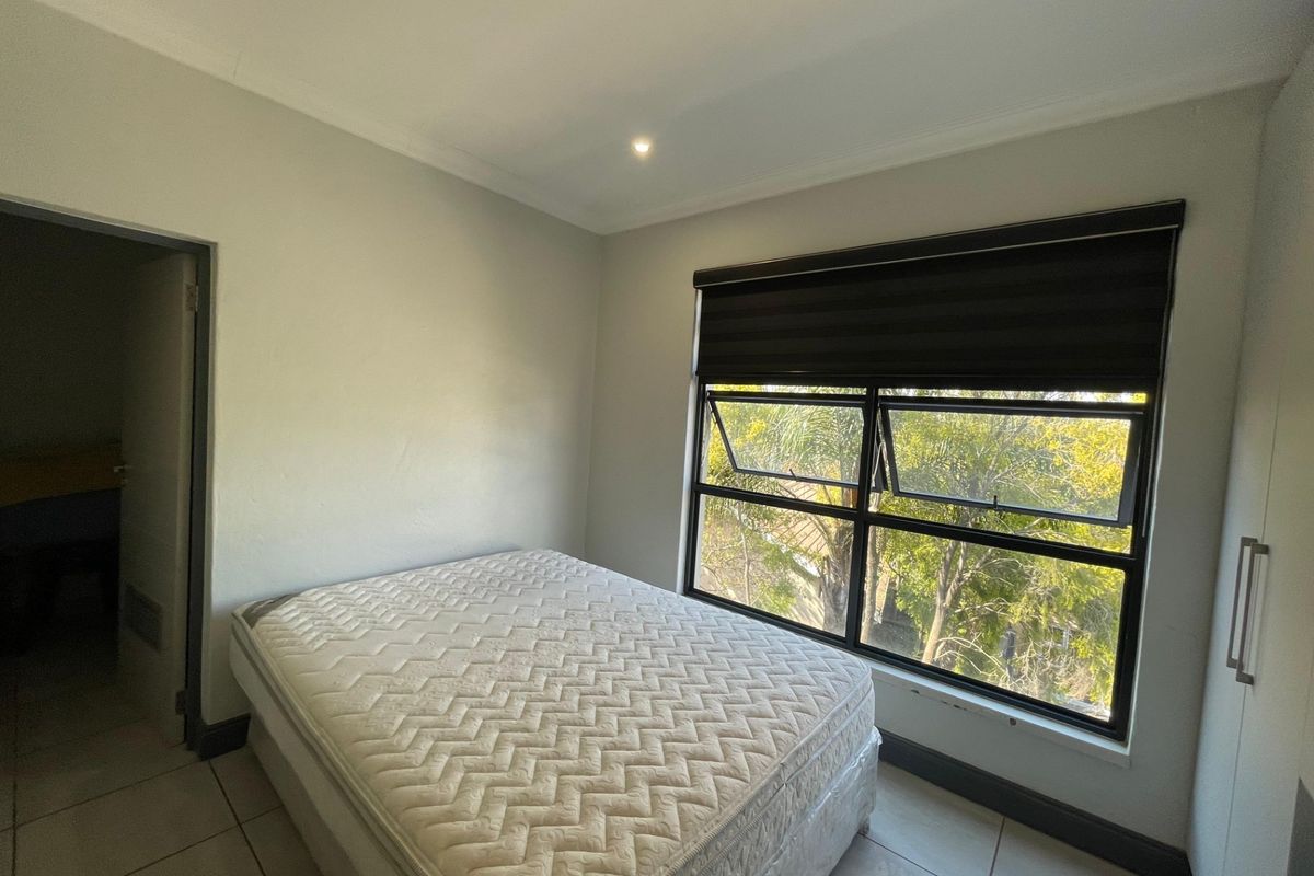 A bedroom featuring tiled flooring, built-in cupboards, and large windows with modern blinds, offering a bright and functional living space.