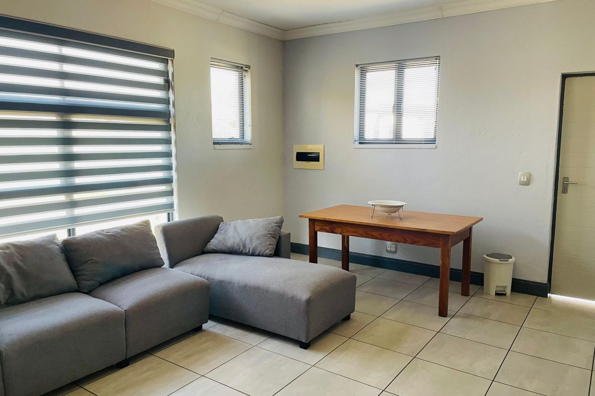 A bright living area featuring neutral tiled flooring, modern zebra blinds, and recessed lighting, offering a clean and functional space.