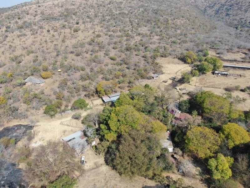 Aerial view of a rural farm property featuring multiple outbuildings with corrugated metal roofs set within a large, wooded landscape.