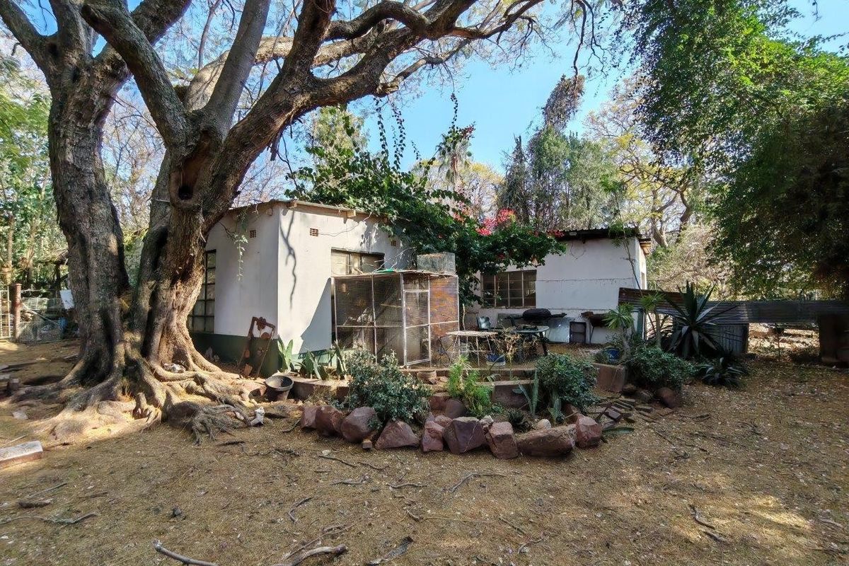 Rear view of a farm dwelling featuring masonry construction, steel-framed windows, and mature trees in a natural garden setting.