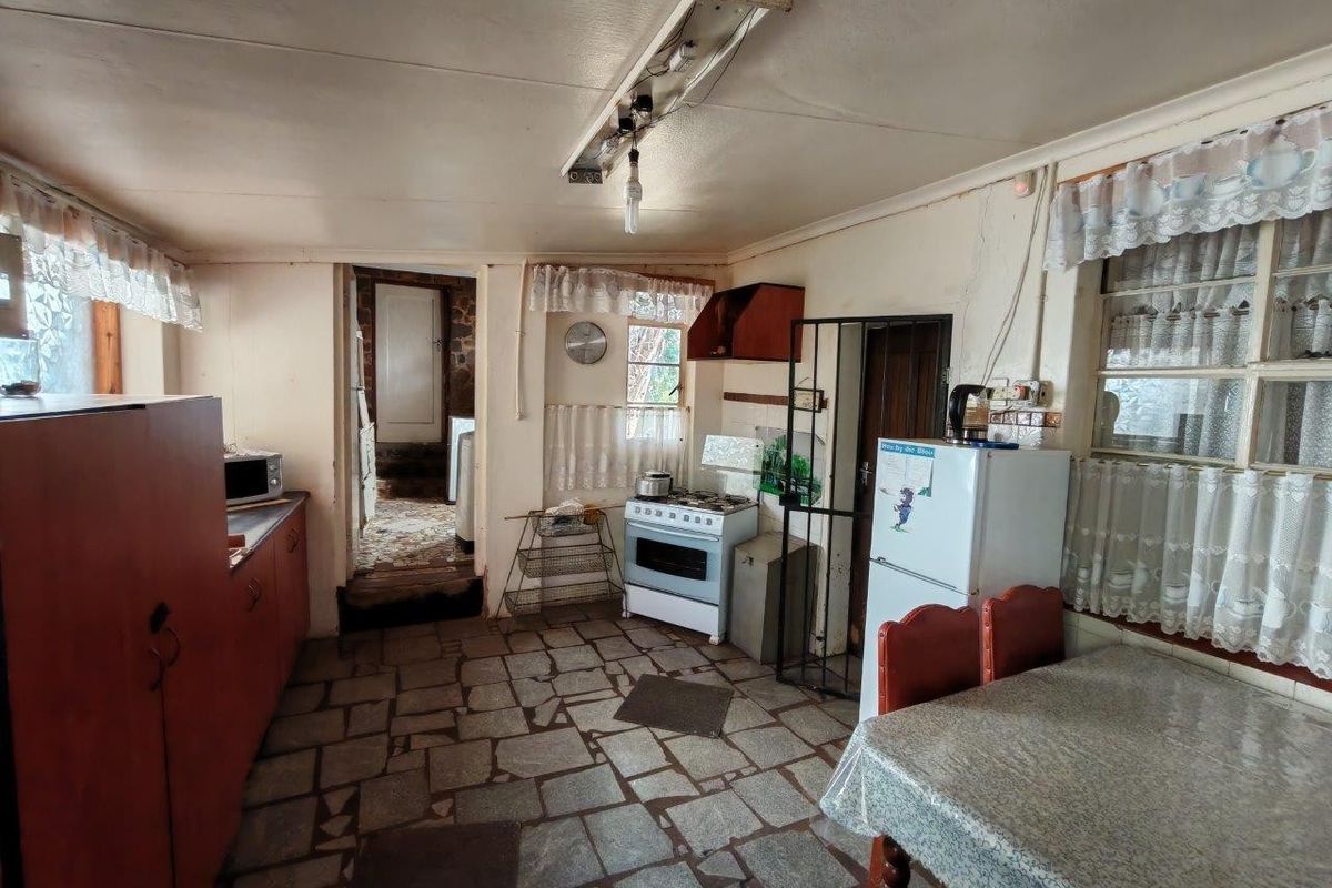 A rustic kitchen featuring stone flooring, built-in cabinetry, and a freestanding stove, offering significant potential for modernization and renovation.