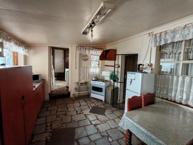 A rustic kitchen featuring stone flooring, built-in cabinetry, and a freestanding stove, offering significant potential for modernization and renovation.