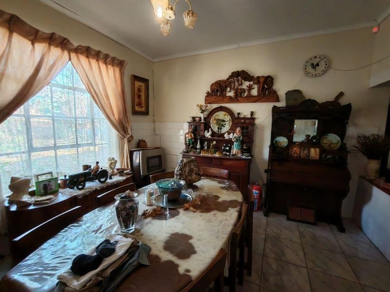A dining room featuring tiled flooring and a large window, providing natural light. The space requires cosmetic updates to modernize the finishes.