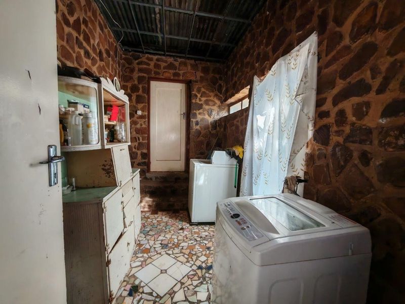 A rustic laundry room featuring distinctive stone wall cladding, mosaic tile flooring, and a corrugated metal ceiling, providing a functional utility space.