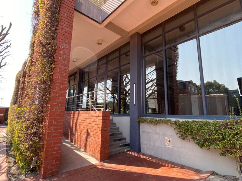 Modern office building exterior featuring a brick facade, large glass windows, and a paved entrance walkway with integrated landscaping.