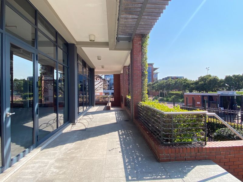 A modern, covered outdoor walkway featuring tiled flooring, brick accents, and large glass office frontage, providing a clean and professional exterior aesthetic.