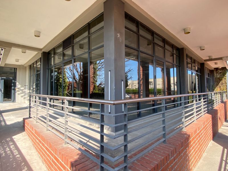 Modern office building exterior featuring a brick facade, large glass windows, and a covered walkway with metal railings.