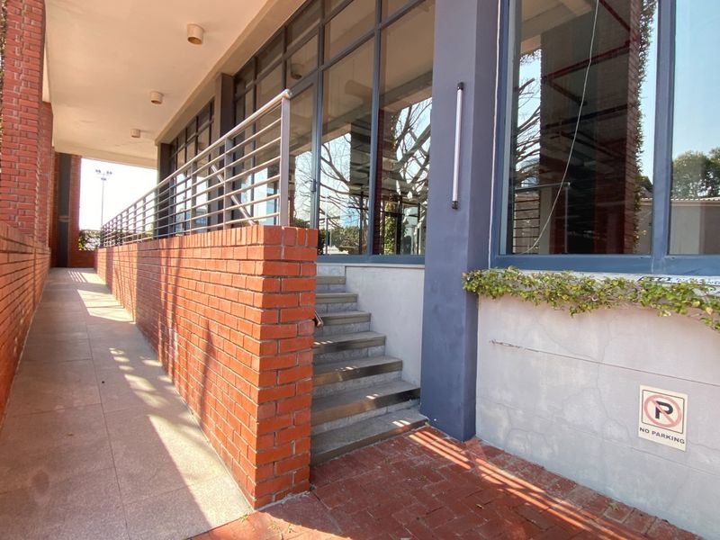 Modern office building exterior featuring a brick retaining wall, stainless steel balustrade, concrete staircase, and expansive glass facade.