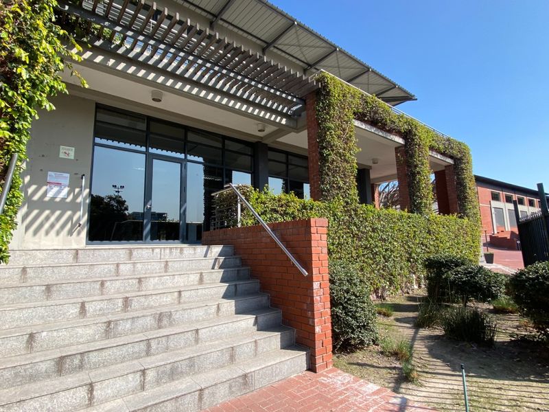Front entrance of the office building featuring stone steps, a brick facade, and a covered pergola with climbing greenery.