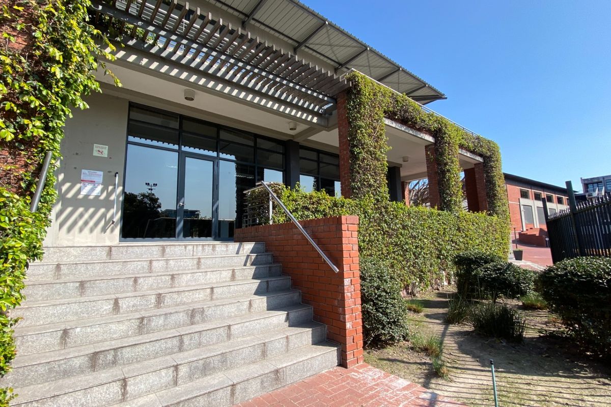 Front entrance of the office building featuring stone steps, a brick facade, and a covered pergola with climbing greenery.