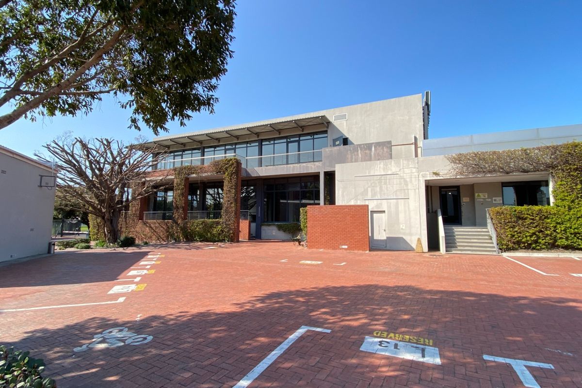 Front view of a modern office building featuring a paved parking area, brick and concrete facade, and large glass windows with balcony access.