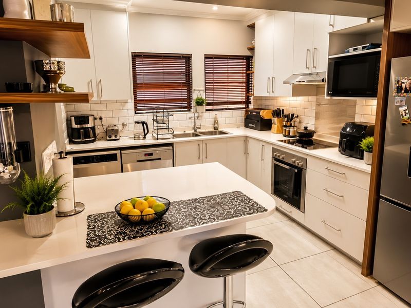 Modern kitchen featuring white cabinetry, stone countertops, subway tile backsplash, integrated appliances, and a functional breakfast bar island.