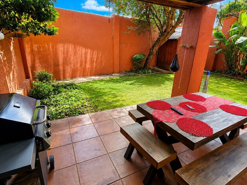 A covered outdoor patio area featuring tiled flooring and masonry pillars, overlooking a private garden with a boundary wall.