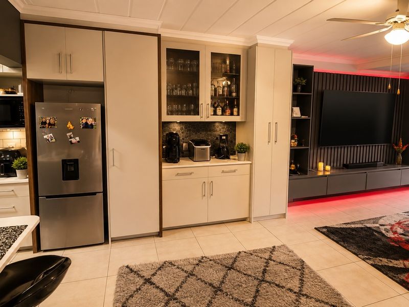 Modern open-plan living area featuring a sleek kitchen with built-in appliances, tiled flooring, and a contemporary media wall with integrated cabinetry.
