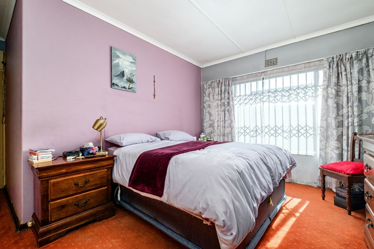 A bedroom featuring a large window with a fitted security gate and a wall-mounted air vent.