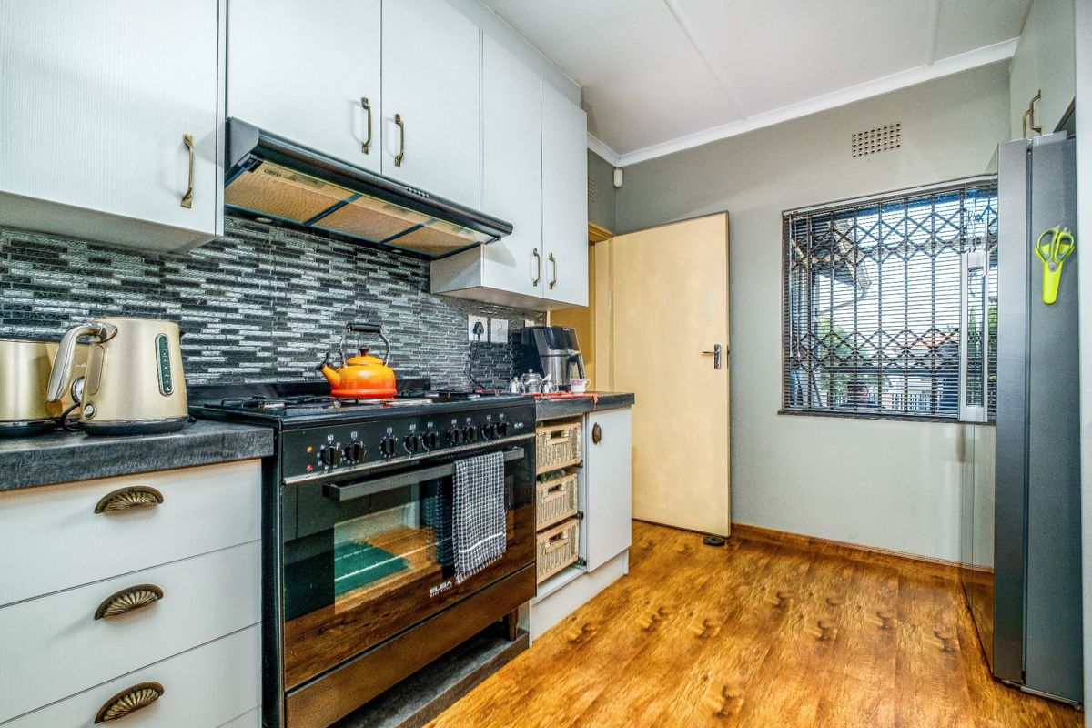 A functional kitchen featuring white cabinetry, a gas stove with extractor fan, modern tiled backsplash, and durable laminate flooring.
