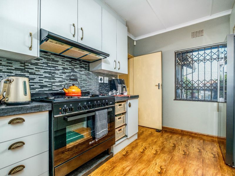 A functional kitchen featuring white cabinetry, a gas stove with extractor fan, modern tiled backsplash, and durable laminate flooring.