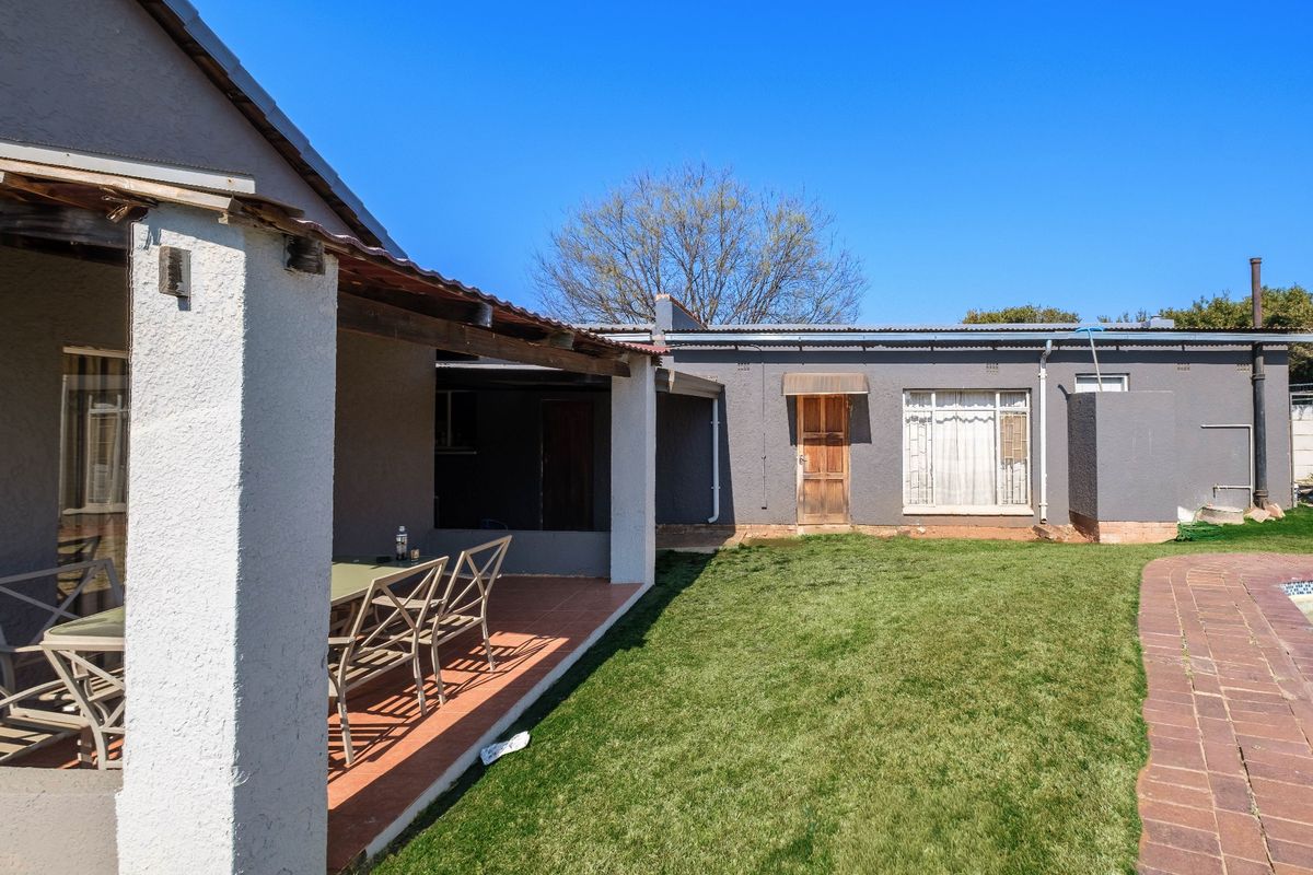 Rear view of the property featuring a covered patio area, a well-maintained lawn, and brick paving leading towards the garden.