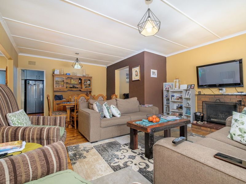 Open plan living and dining area featuring a brick fireplace, hardwood flooring, and exposed beam ceiling, creating a warm and functional family space.