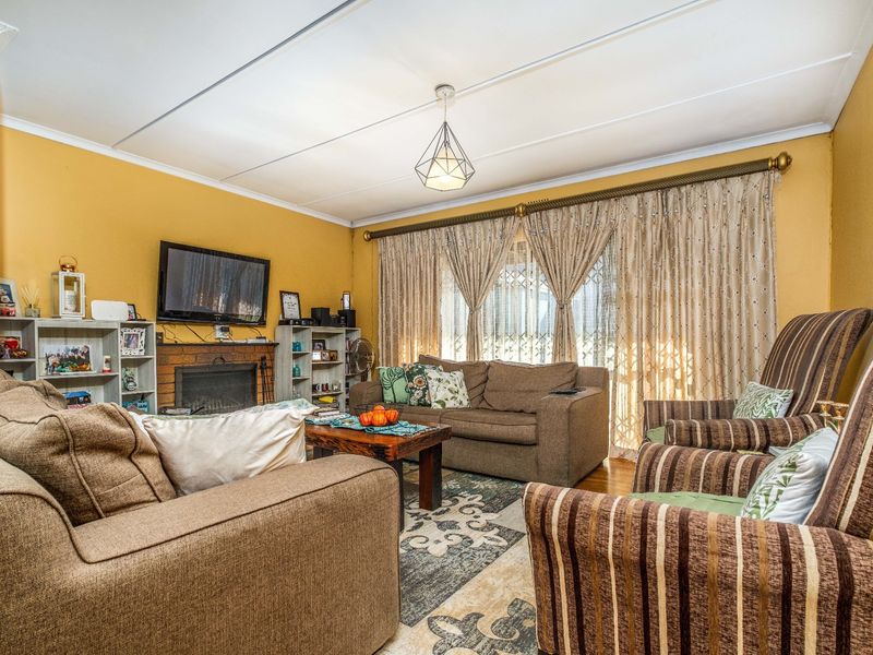 A comfortable living room featuring a brick fireplace, parquet flooring, and large windows with security gates, offering a warm and functional living space.