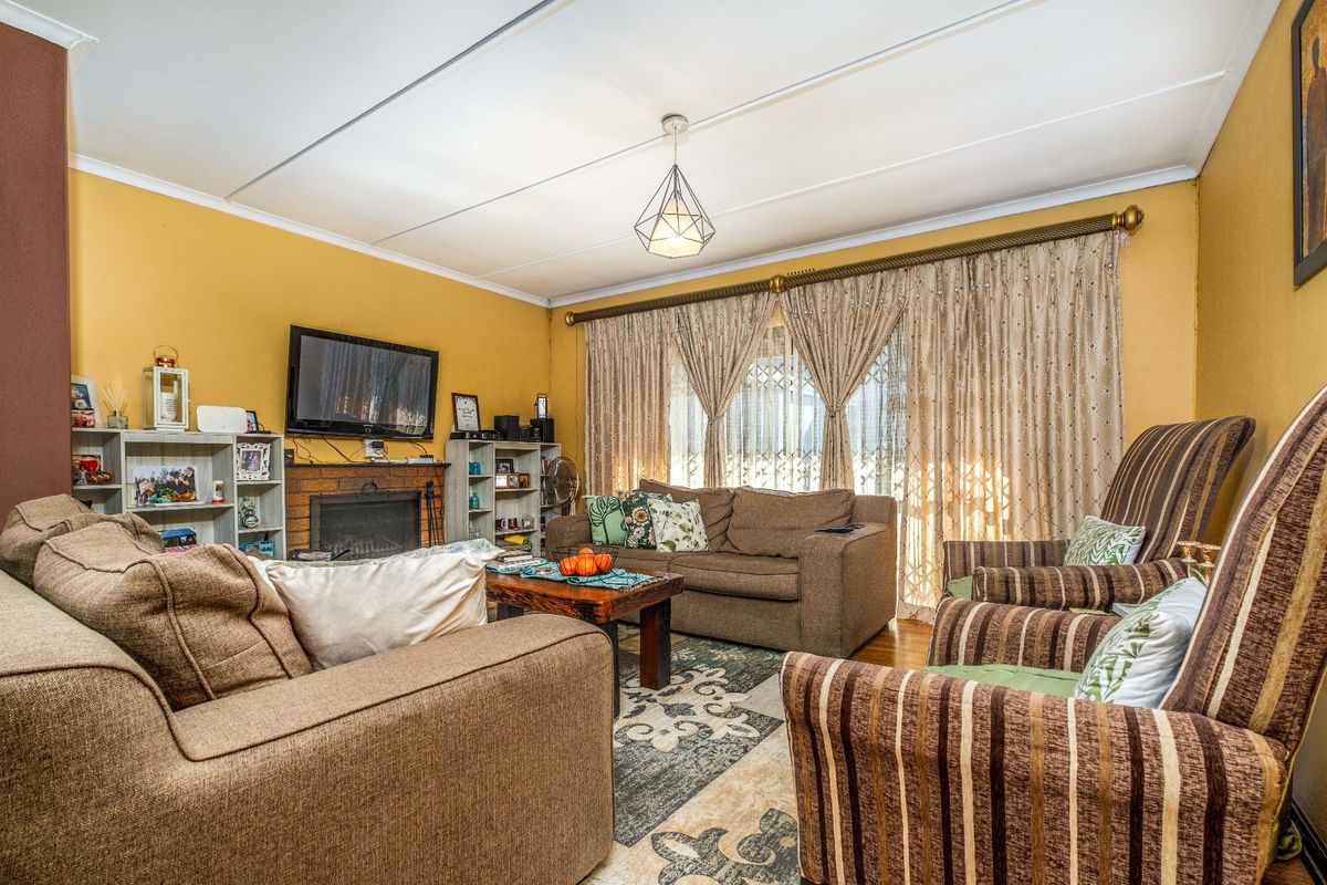A comfortable living room featuring a brick fireplace, parquet flooring, and large windows with security gates, offering a warm and functional living space.