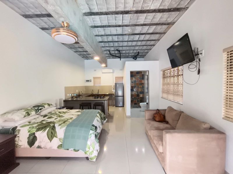 Open-plan studio cottage featuring a modern kitchen with island, exposed concrete ceiling, tiled floors, and an en-suite bathroom.
