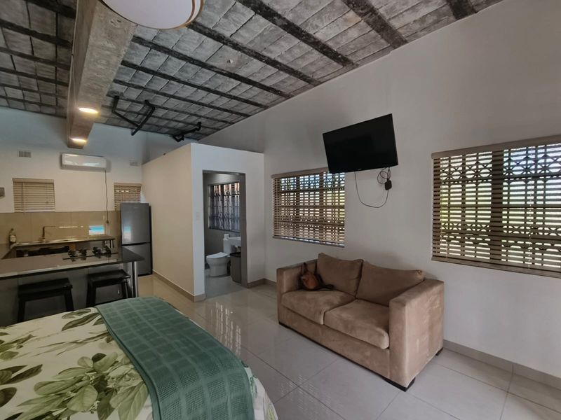 Open-plan studio cottage featuring a modern kitchen island, exposed brick ceiling, tiled flooring, and an integrated bathroom area.