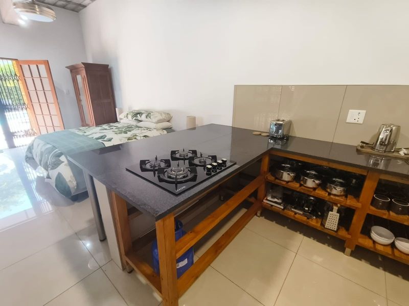 Open-plan studio space featuring a compact kitchen area with a gas hob, stone countertops, and timber shelving, seamlessly integrated with the bedroom area.