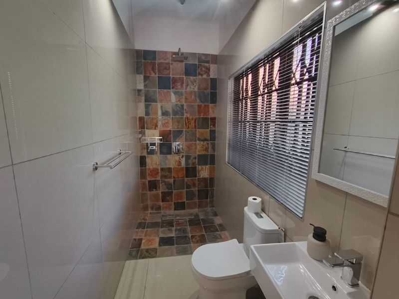 Modern bathroom featuring a walk-in shower with multi-colored stone-look tiles, a white ceramic toilet, and a wall-mounted basin with a sleek mixer tap.